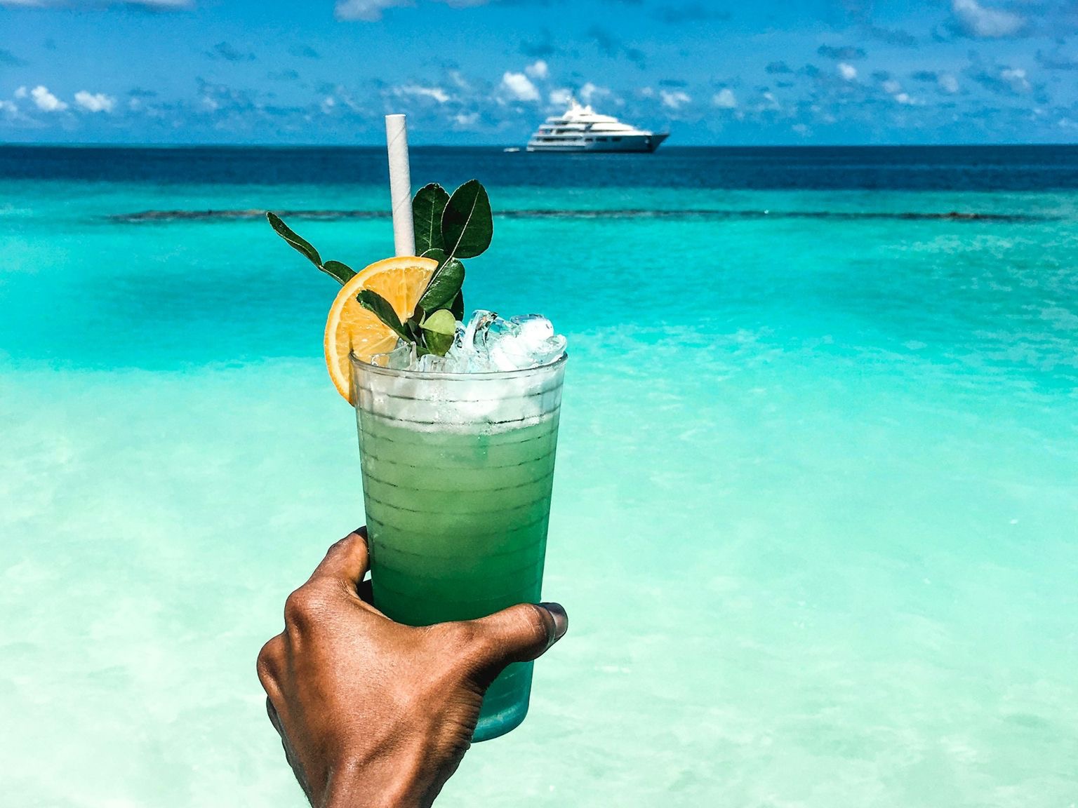 person holding clear drinking glass with green liquid and straw